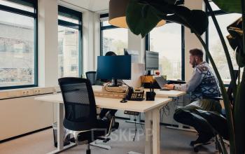 Gezellige kantoorruimte huren op IJsbaanpad 2, Amsterdam De Schinkel. Twee mensen werken aan bureaus met computers in een moderne ruimte met grote ramen.