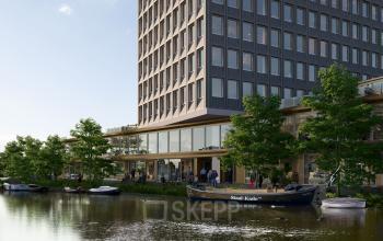 Kantoorpand aan Rijnsburgstraat 9-11, Amsterdam De Schinkel, met glazen gevels en een waterrijke omgeving. Mensen lopen naast het water en een boot ligt aangemeerd bij het kantoor.