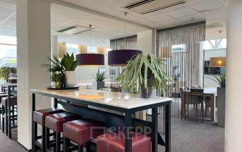 Modern ingericht kantoorpand op Daalwijkdreef 47 in Amsterdam Duivendrecht, met hoge tafels, paarse krukken en groene planten. Geschikt voor kantoorruimte huren met diverse werkruimtes.