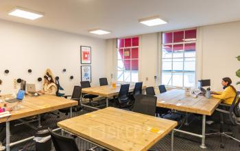 Kantoorruimte huren op Herengracht 420, Amsterdam Grachtengordel, voorzien van grote ramen, werkplekken met stoelen, en mensen aan het werk achter laptops.