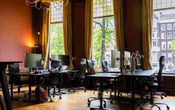 Kantoorruimte huren aan de Keizersgracht 482 in Amsterdam Grachtengordel. Historische kamer met sierlijk plafond, houten vloer, moderne werkplekken en bureaus met computers. Grote ramen bieden uitzicht op de gracht.