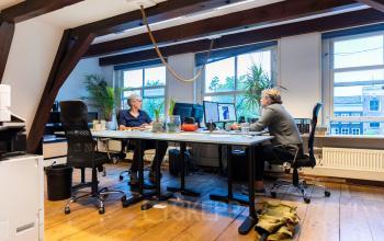 Kantoorruimte huren aan de Keizersgracht 482, Amsterdam Grachtengordel, met twee personen achter bureaus aan het werk, ramen met uitzicht en houten vloeren