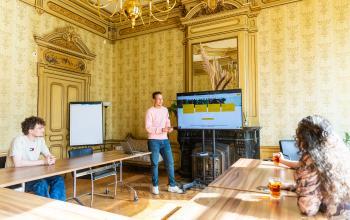 Interieur van het kantoorpand op Keizersgracht 482, Amsterdam Grachtengordel, met vergadertafels, een presentator bij een groot scherm en twee deelnemers aan de bespreking.