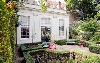 Buitenzijde van een historisch kantoorpand op de Keizersgracht 62 – 64 in Amsterdam Grachtengordel, omgeven door een groene tuin met bankjes, perfect voor een pauze tijdens het kantoorruimte huren.