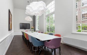Vergaderruimte met kleurrijke stoelen, moderne verlichting en een groot raam, gelegen aan de Keizersgracht in Amsterdam. Ideaal voor kantoorruimte huren in een stijlvolle omgeving.