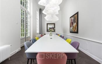 Vergaderruimte in kantoorpand op Keizersgracht 62-64 met lange tafel en kleurrijke stoelen, omringd door grote ramen en moderne kunst aan de muur. Kantoorruimte huren in Amsterdam Grachtengordel.