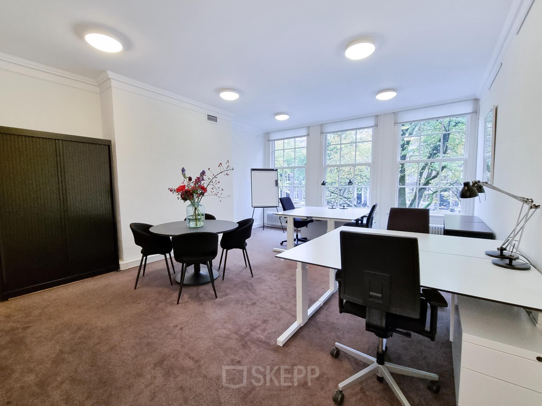 Modern ingerichte kantoorruimte met een vergadertafel, bureaus en uitzicht op de Amsterdamse grachten, beschikbaar voor huur op Keizersgracht 62 – 64.