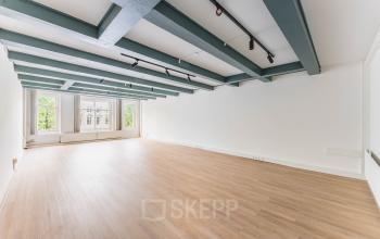 Leeg kantoorpand aan Herengracht 221, Amsterdam Grachtengordel, met houten vloer en balkenplafond, zicht op groene omgeving door grote ramen. Optimaal voor kantoorruimte huren.
