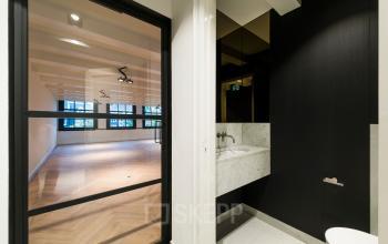 Interieur van een kantoor op Keizersgracht 119 in Amsterdam Grachtengordel, met een lege ruimte en moderne wasbak tegen donkere muur. Veel natuurlijk licht door grote ramen.