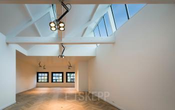 Lichte kantoorruimte op Keizersgracht 119 in Amsterdam met houten visgraatvloer en grote ramen. Moderne verlichting accentueert de hoge plafonds.