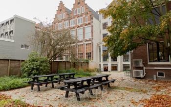 Buitenaanzicht van het kantoorpand aan de Keizersgracht 121, Amsterdam Grachtengordel. Tuin met picknicktafels omringd door groen. Geschikt voor creatieve besprekingen in open lucht.