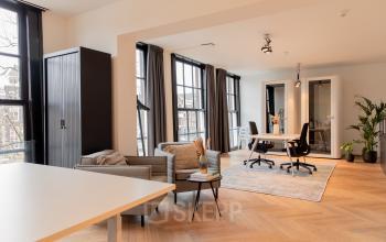 Lichte kantoorruimte met houten vloer en grote ramen aan Keizersgracht 121, Amsterdam Grachtengordel. Moderne inrichting met bureau, stoelen en planten voor een uitnodigende werkomgeving.