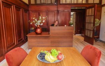 Kantoorpand Herengracht 449 a, Amsterdam Grachtengordel, met houten interieur, receptiebalie waar een persoon werkt, fruitschaal op tafel, bloemenvaas.