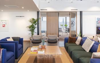 Moderne lounge in het kantoorpand op Stadhouderskade 5-6, Amsterdam Grachtengordel, met comfortabele stoelen en een houten tafel. Ideale ruimte voor informeel overleg of ontspanning tijdens kantooruren.
