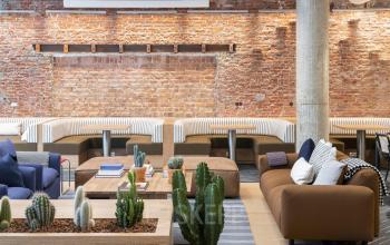 Stijlvolle kantoorruimte huren aan de Stadhouderskade 5-6, Amsterdam Grachtengordel met moderne meubels, comfortabele zitplekken en industriële bakstenen muur.