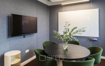 Vergaderruimte in Stadhouderskade 5-6, Amsterdam Grachtengordel, met ronde tafel, groene stoelen, een witte schrijfwand en een hangende flatscreen. Geschikt voor kantoorruimte huren.