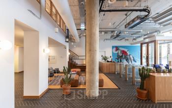 Moderne kantoorruimte huren in Amsterdam Grachtengordel met frisse open inrichting en industriële elementen. Gemeubileerde lounge met stijlvolle zitplekken en planten. Uitstekende locatie voor professionele activiteiten.