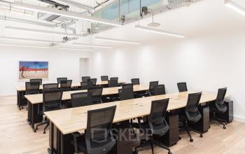 Moderne kantoorruimte op Stadhouderskade 5-6, Amsterdam met lange houten tafels en zwarte stoelen, ideaal voor open werkruimtes. Perfect om te huren in de Amsterdam Grachtengordel.