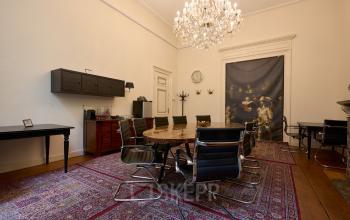Kantoorruimte huren op Keizersgracht 391A, Amsterdam Grachtengordel. Elegante vergaderruimte met grote houten tafel, zwarte stoelen en een prachtige kroonluchter aan het plafond.