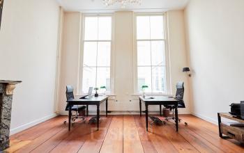 Lichte kantoorruimte op Keizersgracht 391A, Amsterdam Grachtengordel, met houten vloeren, hoge ramen en twee werkplekken met bureaustoelen en tafels. Ideaal om een kantoorpand te huren.