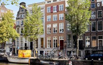 Een rij historische grachtenpanden langs de Keizersgracht in Amsterdam, met aan de waterkant een aantal fietsen en een boot.