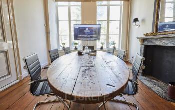 Kantoorruimte huren aan de Keizersgracht 391A in Amsterdam Grachtengordel met een authentieke vergadertafel, stoelen rondom en een flatscreen. De ruimte heeft een karakteristieke houten vloer en grote ramen.