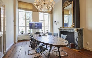 Kantoorruimte aan de Keizersgracht 391A, Amsterdam Grachtengordel met houten vloer, ovale tafel en luxe kroonluchter. Geschikt voor vergaderingen met natuurlijke verlichting en stijlvolle inrichting.