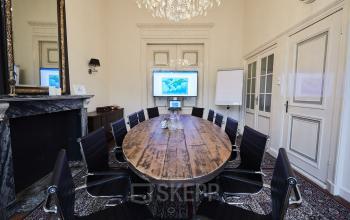 Kantoorruimte huren aan de Keizersgracht 391A in Amsterdam Grachtengordel, met een stijlvolle vergadertafel, chique stoelen en een beeldscherm, voorzien van een klassieke open haard en kroonluchter.