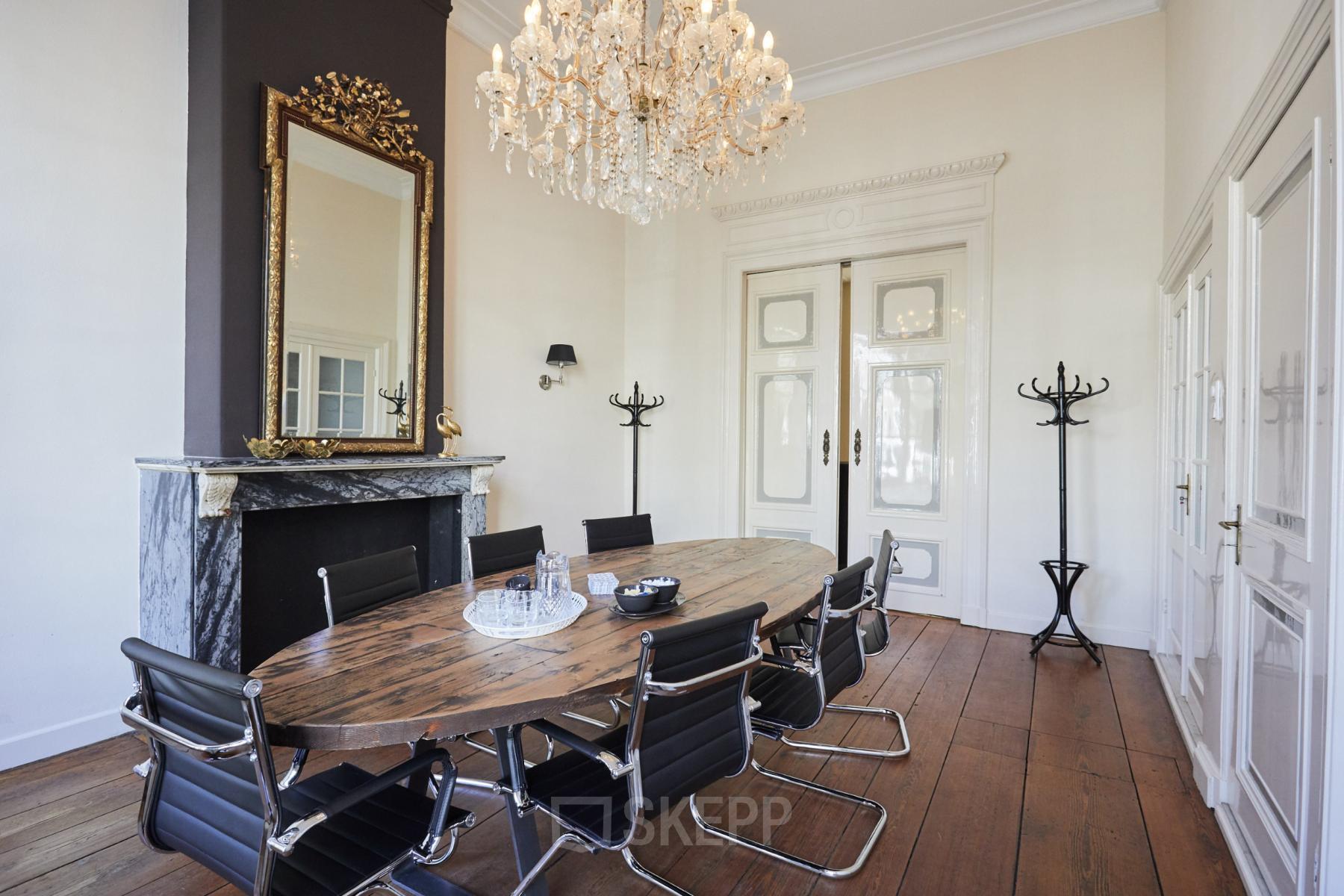 Stijlvolle vergaderruimte in een kantoorpand aan de Keizersgracht 391A, Amsterdam Grachtengordel, met houten tafel, designstoelen en een sierlijke kroonluchter. Ideaal voor kantoorruimte huren met karakter.