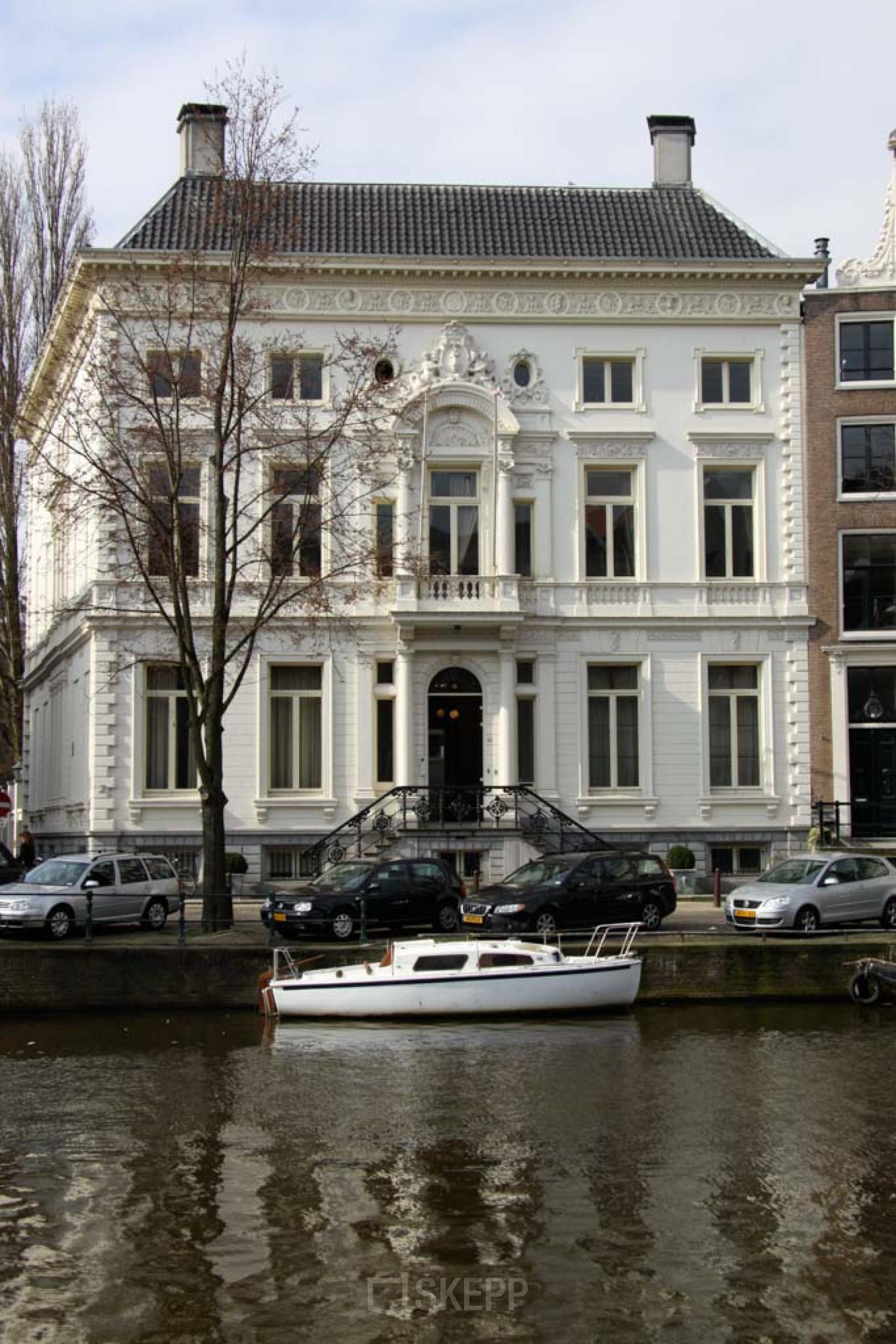 Kantoorpand aan de Keizersgracht 452, Amsterdam Grachtengordel. Klassiek pand met witte gevel, geparkeerde auto's en een boot aan de kade.