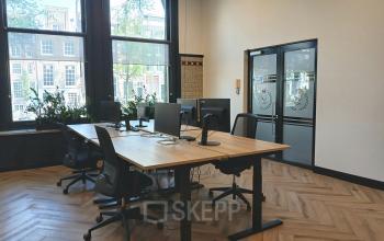 Kantoorruimte te huur aan de Herengracht 320 in Amsterdam Grachtengordel, met moderne bureaus en stoelen bij grote ramen met uitzicht op grachtenpanden.