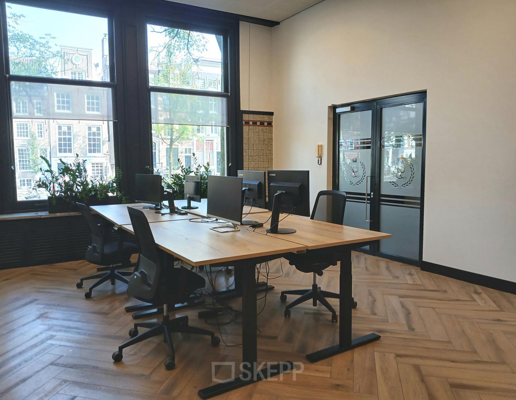 Kantoorruimte te huur aan de Herengracht 320 in Amsterdam Grachtengordel, met moderne bureaus en stoelen bij grote ramen met uitzicht op grachtenpanden.