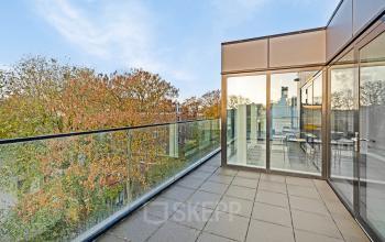 Buitenzicht op een moderne kantoorpand met glazen balustrade en weerspiegeling van bomen in de glazen gevel, gelegen aan de Keizersgracht 572 572 in Amsterdam Grachtengordel.