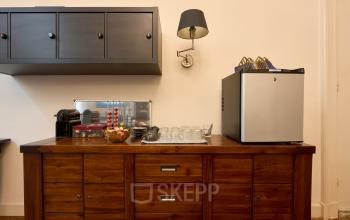 Chique ingerichte pantry met houten dressoir, koffiemachine, glaswerk en klein koelkastje in het kantoorpand op Keizersgracht 391A, Amsterdam Grachtengordel. Ideaal voor kantoorruimte huren met stijl.