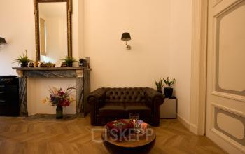 Gezellige kantoorruimte te huur aan de Keizersgracht 391A, Amsterdam, met een klassieke leren bank, marmeren schouw en houten vloer, ideaal voor inspirerende ontmoetingen.