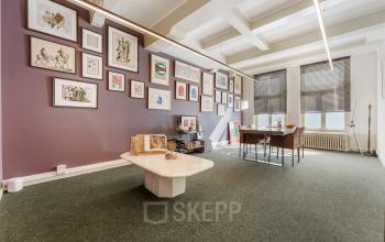 Ruime en lichte kantoorruimte op Keizersgracht 261 in Amsterdam Grachtengordel met kunstwerken aan de paarse muur, twee bureaus en een lage tafel.