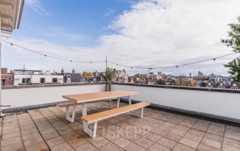 Dakterras in Amsterdam Grachtengordel met houten tafel en banken, uitzicht op de stad. Ideaal voor ontspanning tijdens kantooruren in dit kantoorpand aan de Herengracht 582-584.