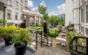 Buitenterras van het kantoorpand aan de Herengracht 459-469 in Amsterdam Grachtengordel, met tafels en stoelen te midden van groene planten en bloembedden.