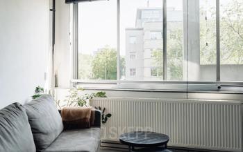 Lichte kantoorruimte op Weesperstraat 394-396 in Amsterdam Grachtengordel met een grijze bank en nesttafeltjes bij het raam. Ideaal voor ontspannende pauzes tijdens het huren van deze kantoorpand.