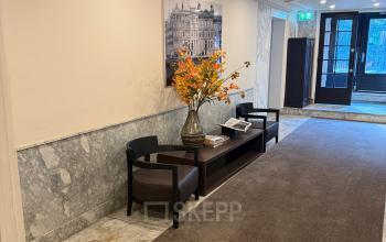 Lichte receptieruimte met marmeren details op Herengracht 493, Amsterdam. Twee stoelen en een tafel met bloemen geven een gastvrije uitstraling. Geschikt voor kantoorruimte huren.