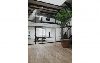 Moderne kantoorruimte huren op Herengracht 168, Amsterdam Grachtengordel, met glazen wanden en een lichte houten vloer. Grote planten en een open indeling creëren een inspirerende werkomgeving.