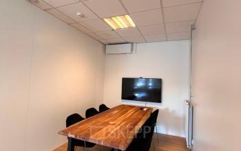 Vergaderkamer met houten tafel, meerdere stoelen en een muurbeeldscherm in een kantoorpand op Amstel 62, ideaal voor wie kantoorruimte wil huren in Amsterdam Grachtengordel.