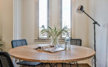 Moderne en lichte vergaderruimte binnen een kantoorpand aan Amstel 62, met een ronde houten tafel, comfortabele stoelen en stijlvolle staande lamp.