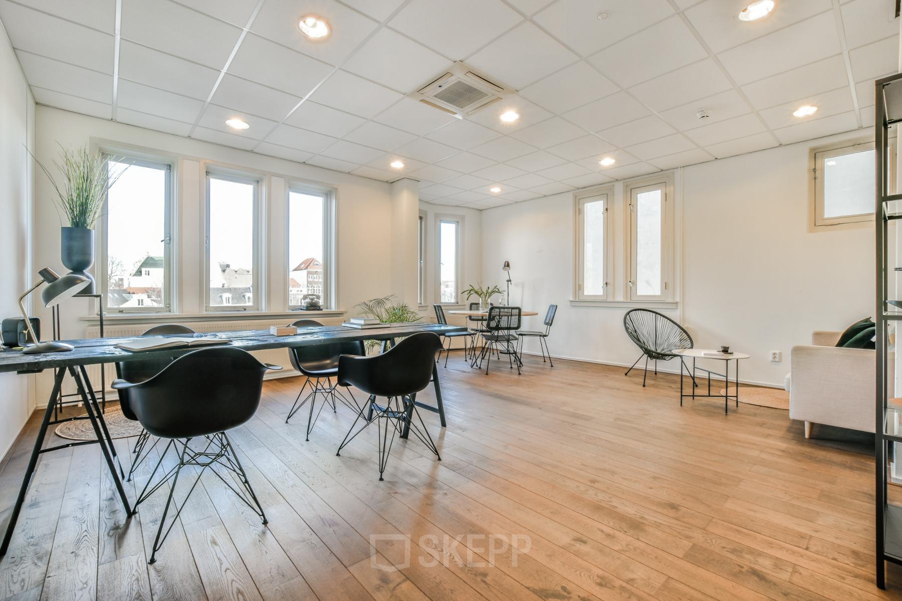 Modern ingerichte kantoorruimte met houten vloer, zwarte stoelen en bureau, planten en heldere belichting, gelegen aan Amstel 62, Amsterdam Grachtengordel.