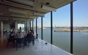 Mensen zitten aan een tafel in een ruim, modern kantoor aan de Moermanskkade 109-113, Amsterdam Houthavens, met uitzicht op het water, ideaal voor kantoorruimte huren.