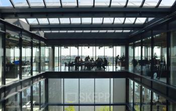 Zakelijke bijeenkomst in modern kantoorpand aan de Moermanskkade 109-113, Amsterdam Houthavens, met glazen dak en uitzicht op het water. Veel daglicht, geschikt voor kantoorruimte huren.