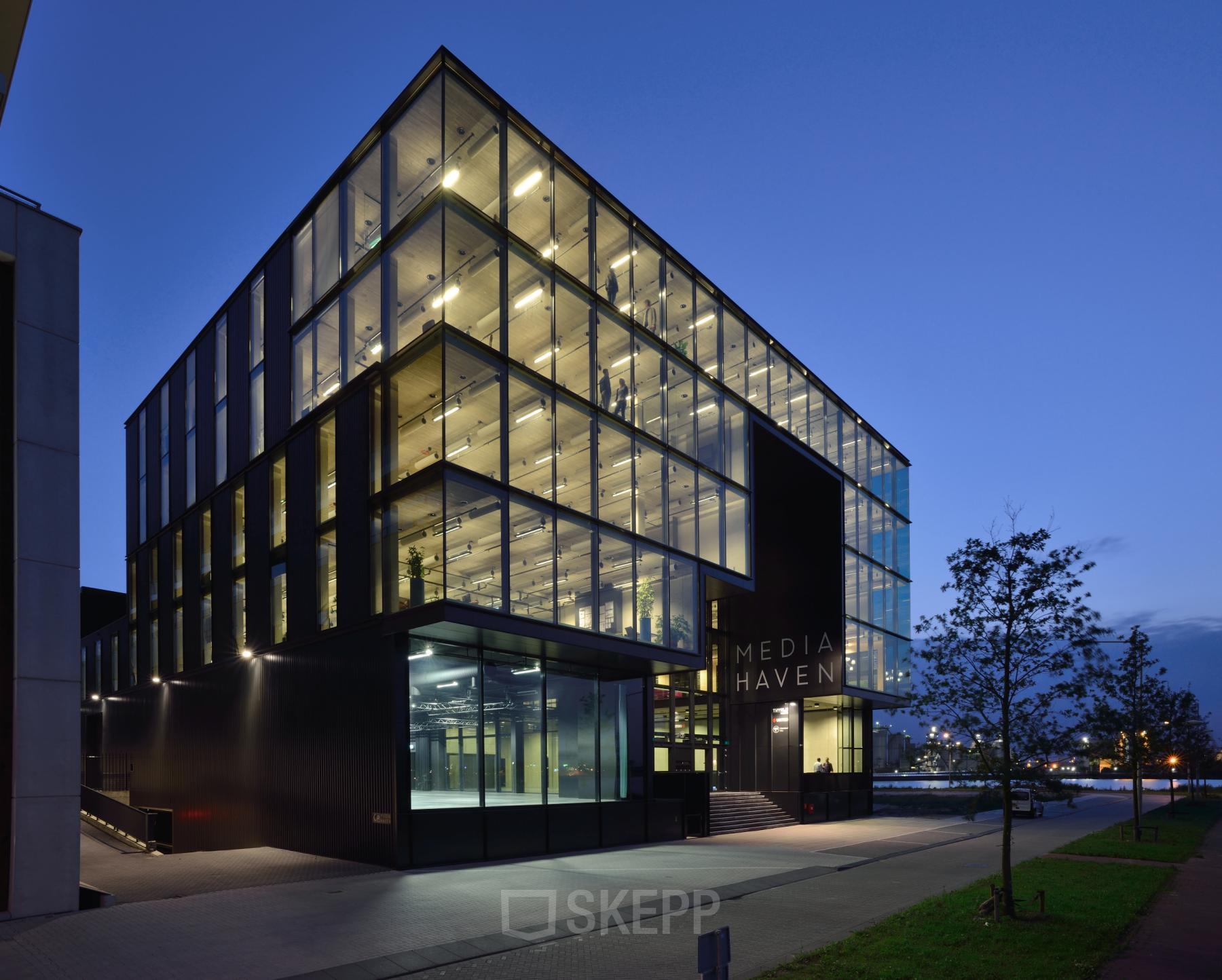 Modern kantoorgebouw aan de Moermanskkade 109-113 in Amsterdam Houthavens, met een glazen gevel verlicht in de schemering. Geschikt voor bedrijven die kantoorruimte willen huren.