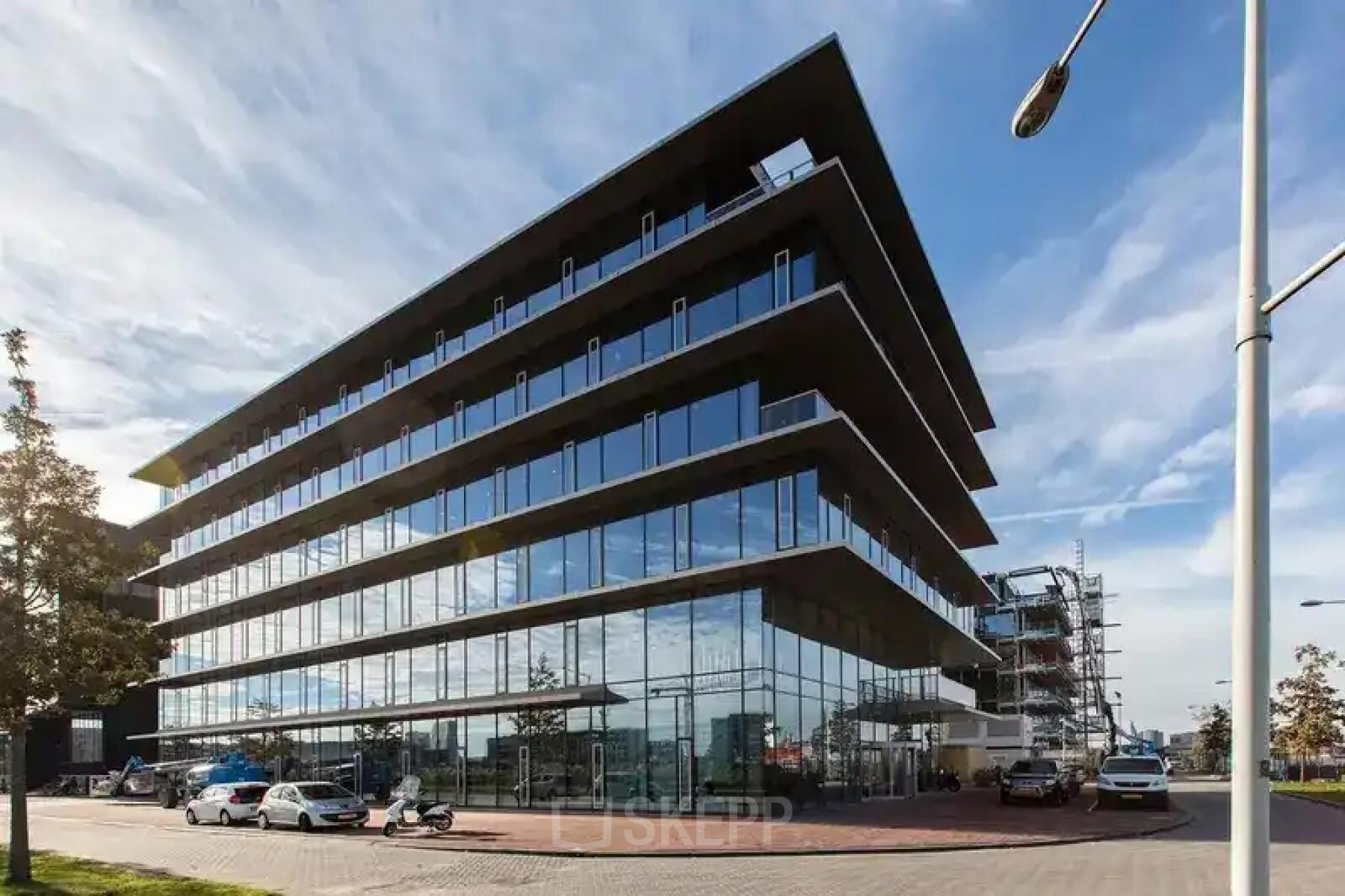 Modern kantoorpand op de Moermanskkade 303 in Amsterdam Houthavens, ideaal voor kantoorruimte huren. Het glazen gebouw weerspiegelt de lucht, met enkele auto's voor het pand geparkeerd.