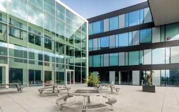 Ruime binnenplaats van het kantoorpand op Pedro de Medinalaan 1-9, Amsterdam IJburg, met moderne glazen gevels en meerdere zitplekken, ideaal voor bedrijven die kantoorruimte willen huren.