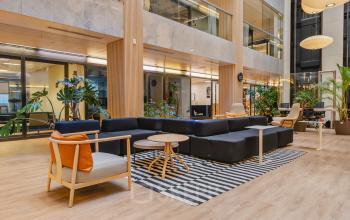 Modern ingerichte kantoorpand op Koningin Wilhelminaplein 1, Amsterdam Nieuw-West met comfortabele zithoek en veel natuurlijke lichtinval. Een uitnodigende ruimte voor werk en overleg, ideaal om kantoorruimte te huren.